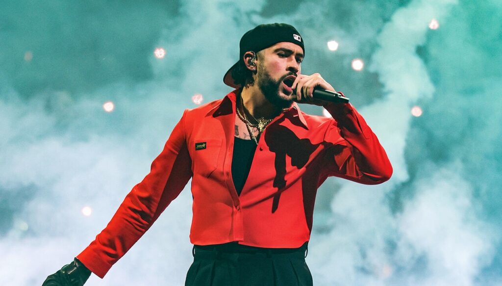 A performer in a red jacket and black beanie singing energetically on stage, surrounded by dramatic smoke and lighting, in a style inspired by Bad Bunny’s live concert aesthetic.
