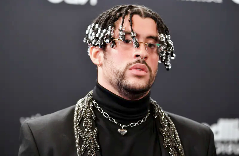 Stylish portrait of a man with braided hair decorated with beads, wearing a black turtleneck and silver chain accessories, in a fashion look inspired by Bad Bunny style.