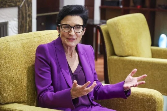 Jane Fraser sitting in a purple suit during a business discussion, showcasing leadership and executive presence, focus keyword Jane Fraser.