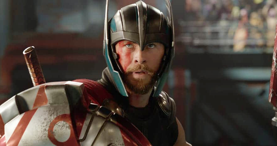 A warrior-like man in futuristic battle armor holding a large shield, with face paint and a determined expression, styled similar to Chris Hemsworth in an action scene.