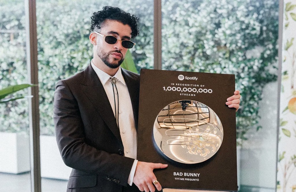 A person holding a large Spotify award plaque, dressed in a dark suit and sunglasses, in a scene inspired by Bad Bunny’s signature style and branding.
