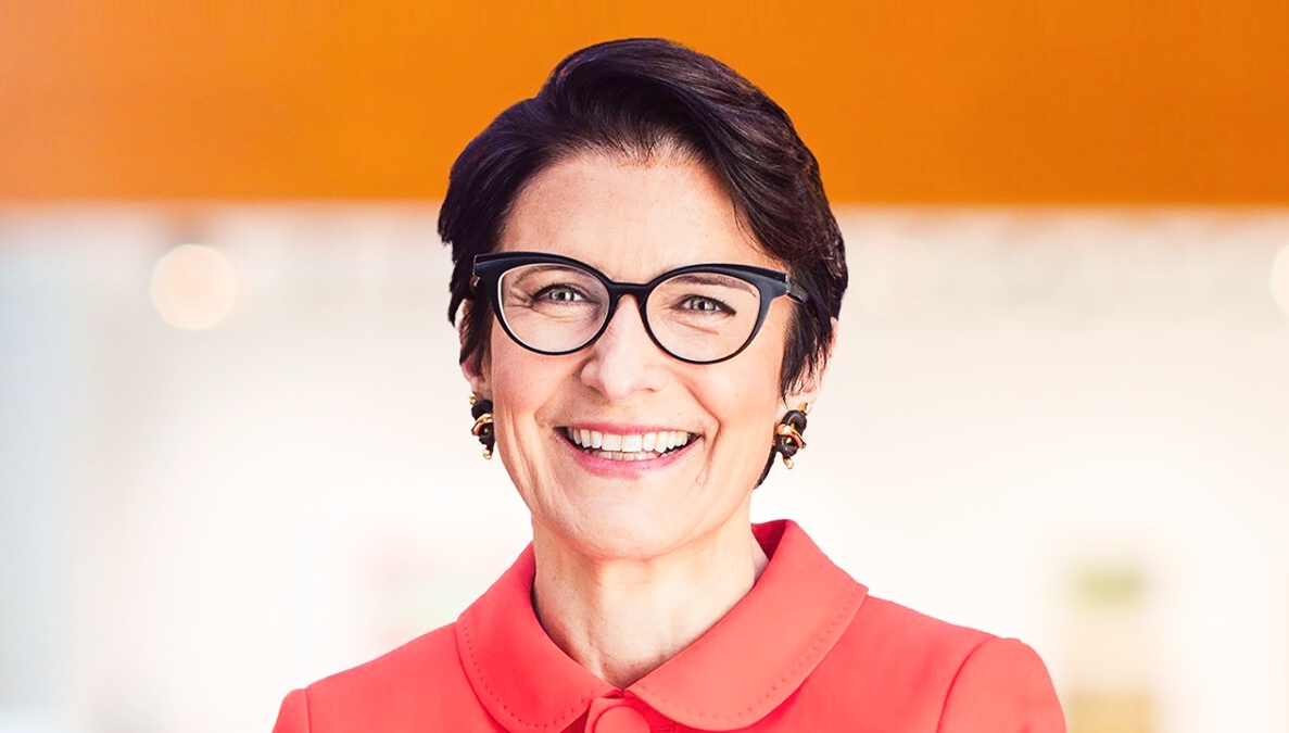 Jane Fraser in a professional portrait wearing glasses and a red suit, representing powerful business leadership and corporate success, focus keyword Jane Fraser.