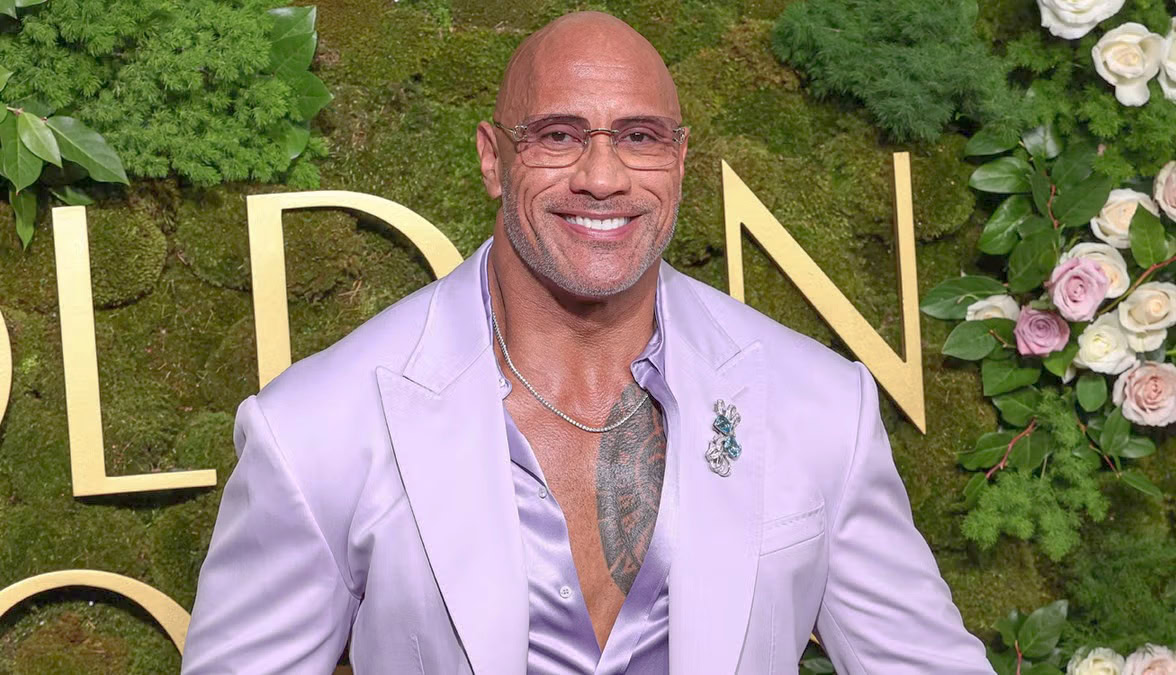 dwayne johnson Smiling bald man in a stylish lavender suit posing confidently on a floral red carpet backdrop.”