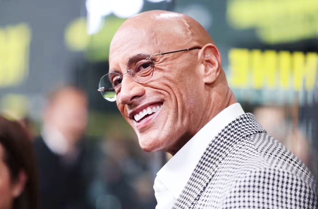 Close-up of a cheerful, well-dressed man in a patterned suit jacket on a red carpet.