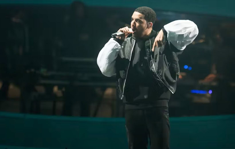A dynamic photo of rapper Bow Wow performing live on stage. He is holding a microphone, wearing a stylish black and white outfit, and passionately engaging the audience under dramatic concert lighting — perfect for a post about Bow Wow’s net worth, music career, or live performances.