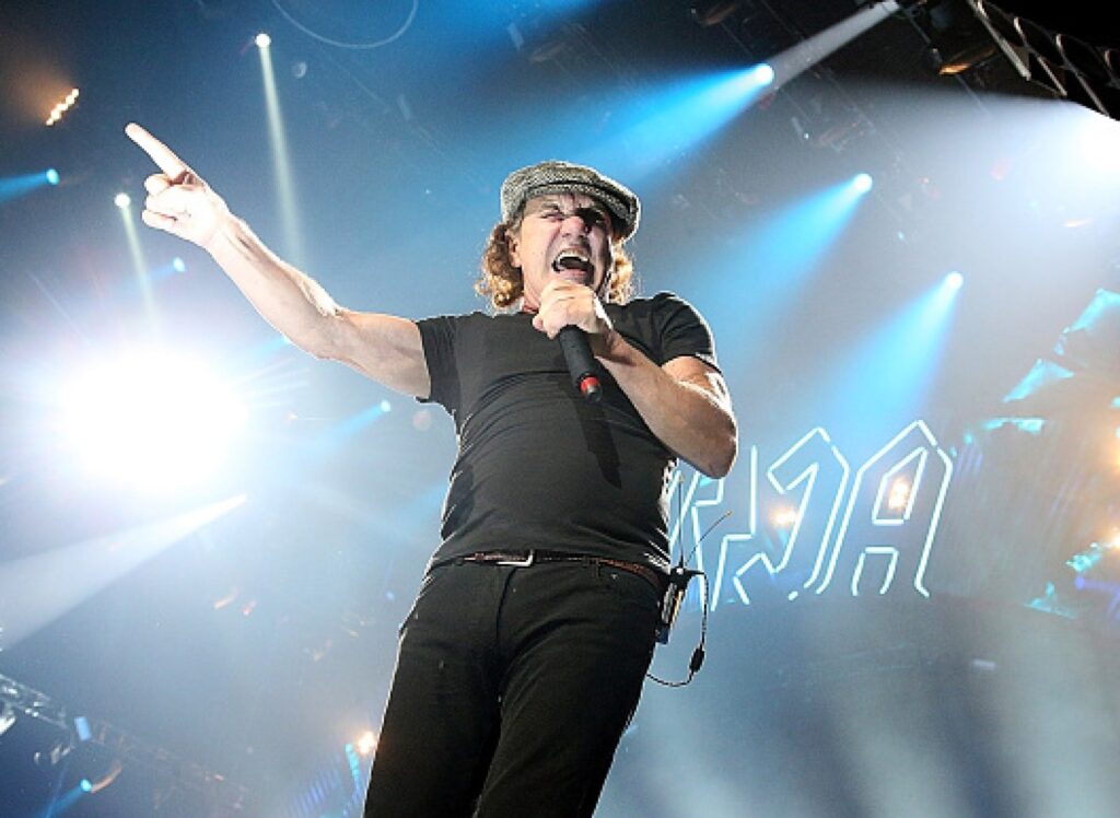 Brian Johnson commands the stage with AC/DC’s iconic lightning bolt logo glowing behind him, delivering high-voltage vocals and raw energy during the 2025 Power Up Tour.