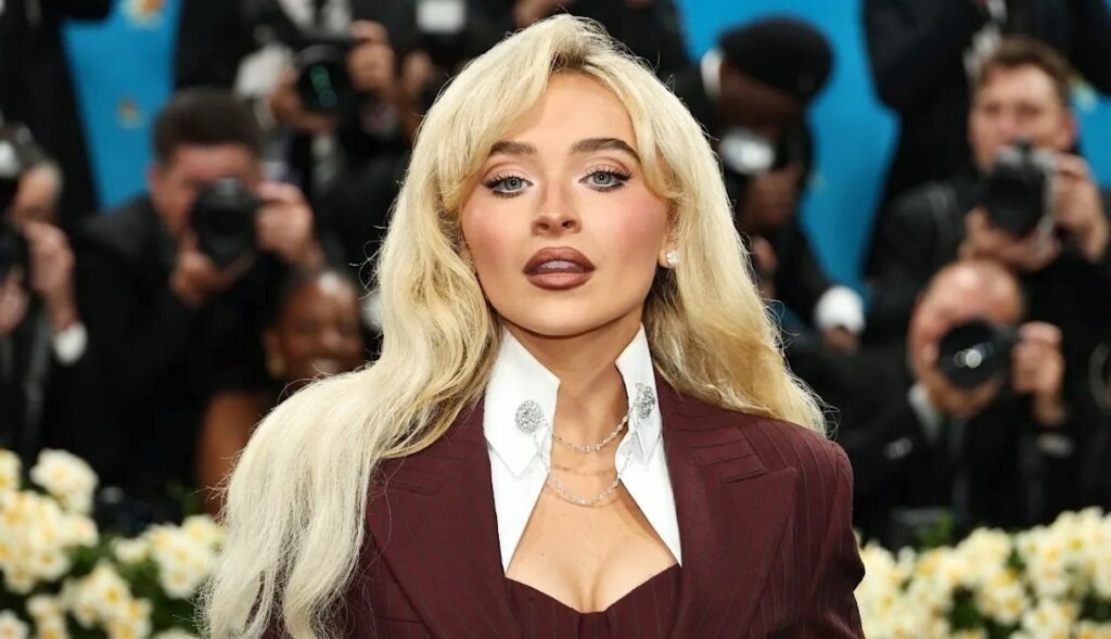 A glamorous blonde woman posing on a red carpet with cameras in the background, used as style inspiration for Sabrina Carpenter–related content.
