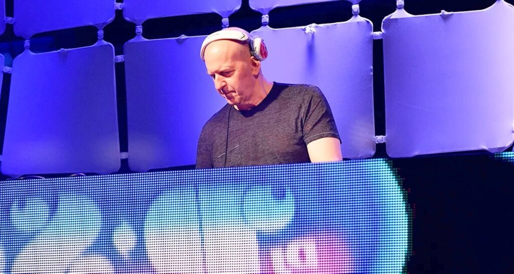 An executive in a dark suit and red patterned tie speaks during an interview, gesturing with his hand in a modern corporate office. Suitable for articles or discussions related to David Solomon, leadership, or finance.