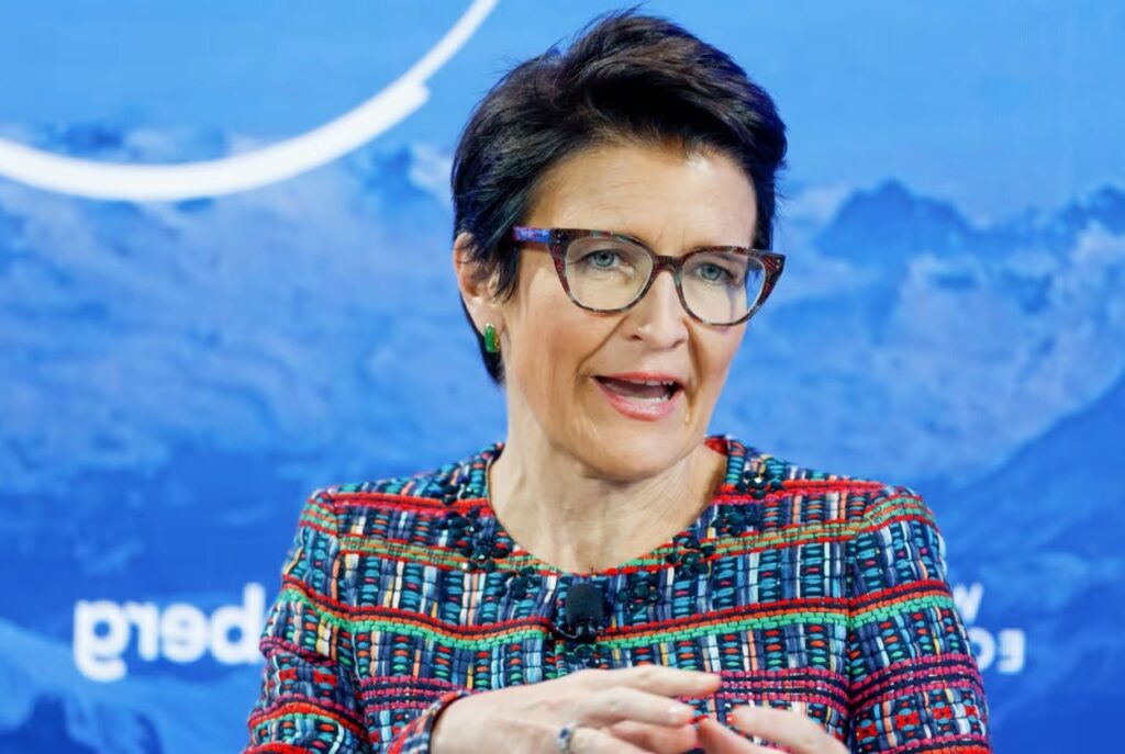 Jane Fraser speaking at a business conference, wearing a colorful suit and glasses, highlighting leadership and global finance influence, focus keyword Jane Fraser.