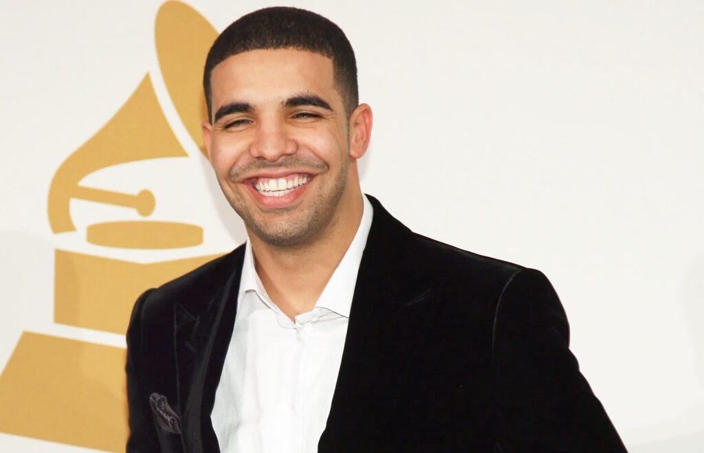 A smiling man dressed in a black suit jacket and white shirt poses in front of a large golden award-themed backdrop.