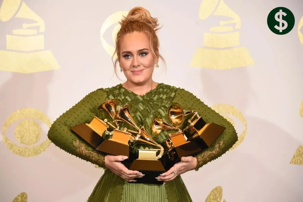 Adele holding multiple Grammy Awards at an awards ceremony, reflecting her record-breaking success, achievements, and Adele Net Worth.