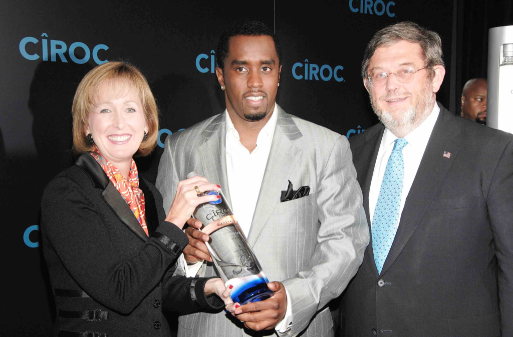Three unidentified people posing at a Cîroc promotional event, holding a bottle together, used for an article discussing p diddy net worth and business ventures.
