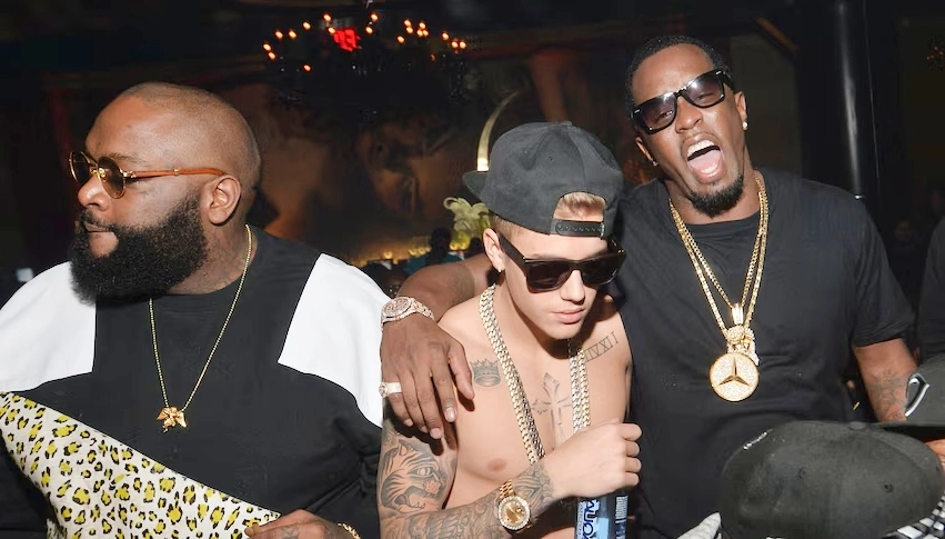 Three unidentified men wearing sunglasses and gold chains at a lively party scene, used for an article discussing p diddy net worth and lifestyle.