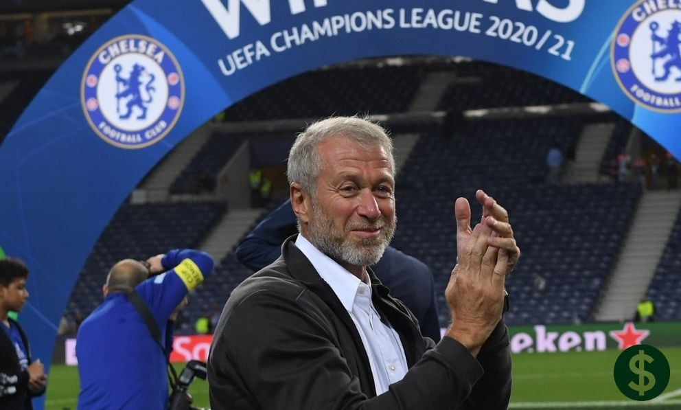 A man clapping inside a football stadium with UEFA Champions League signage in the background, used for an article about Roman Abramovich Net Worth.