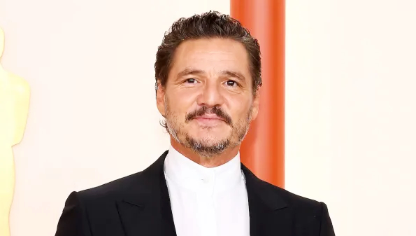 A well-dressed man in a formal suit posing on a red carpet backdrop, used for an article discussing Pedro Pascal Net Worth.