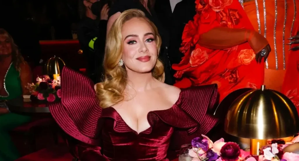 Adele at a high-profile event wearing a burgundy gown, showcasing her success as a Grammy-winning singer and highlighting Adele net worth from music, tours, and albums.